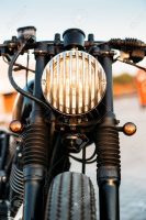 One vintage custom motorcycle cafe racer motorbike with grill headlight on empty rooftop parking lot during sunset. Hipster lifestyle, student dream. Lamp is on and directed to camera.